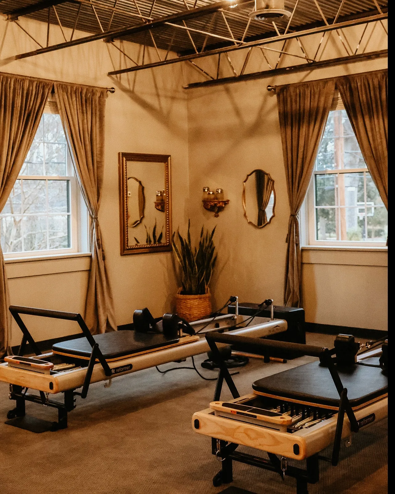 The warm boutique reformer studio interior with wood-framed machines, gold curtains, and antique mirrors